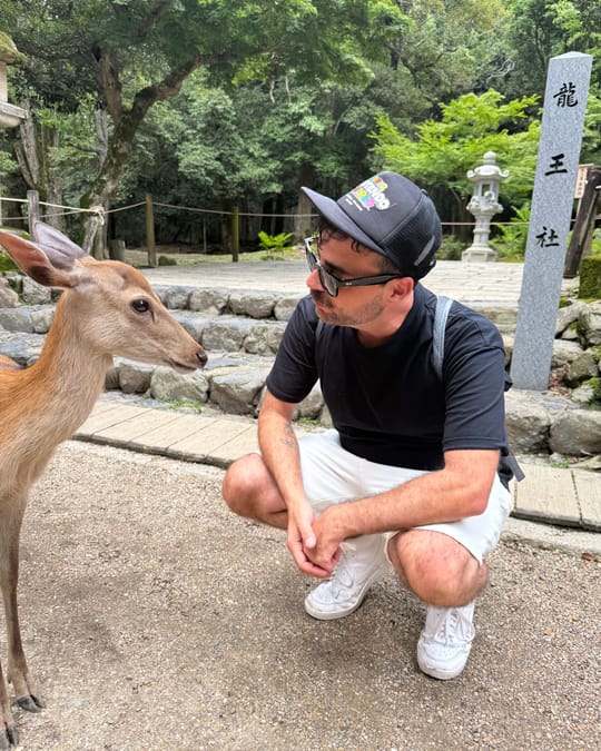 Kris crouching face to face with a deer on a gravel path.