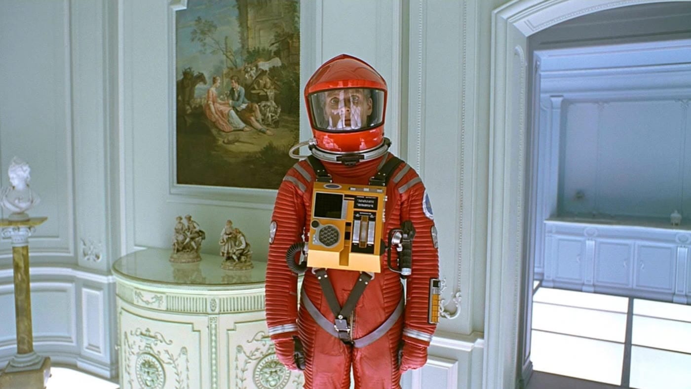 An astronaut in a red spacesuit stands in an ornate white bedroom near the end of 2001.