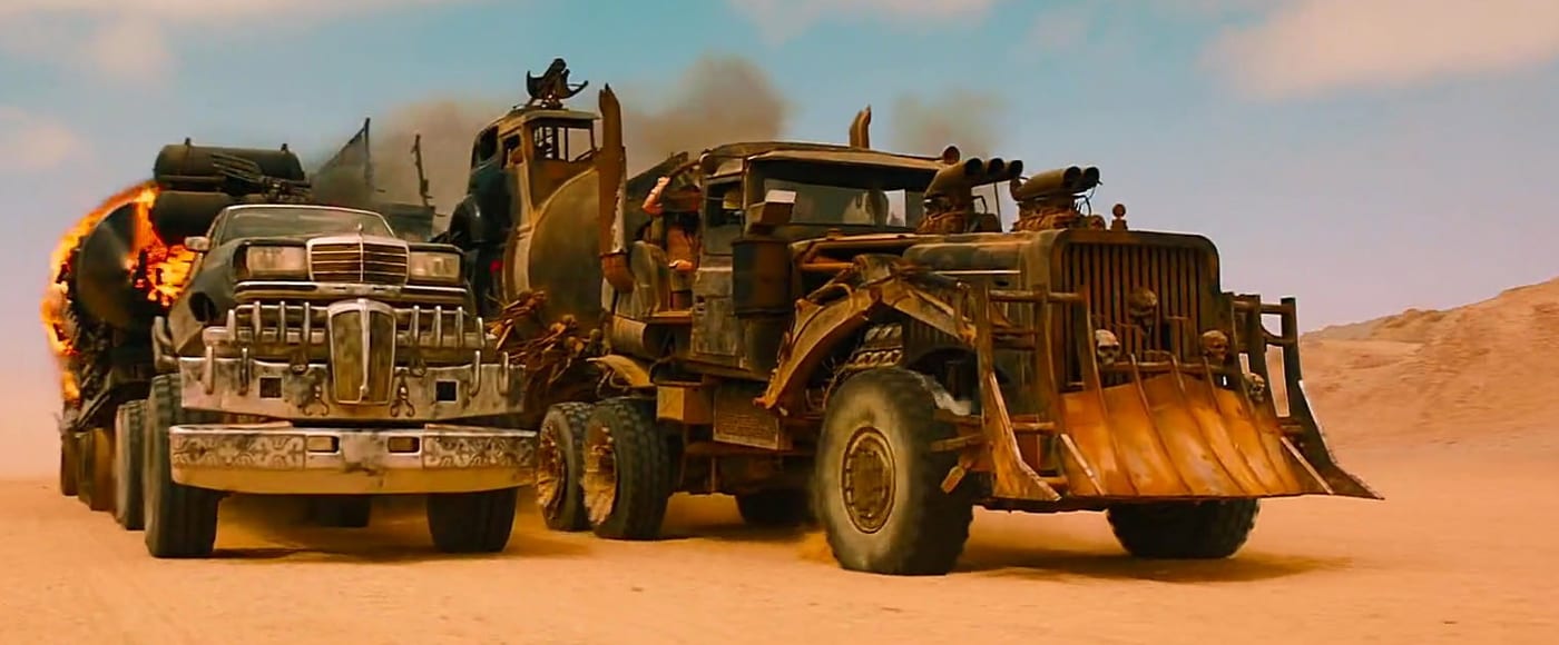 The War Rig races back across the sand beside a chrome-grilled tanker whose rear is on fire.