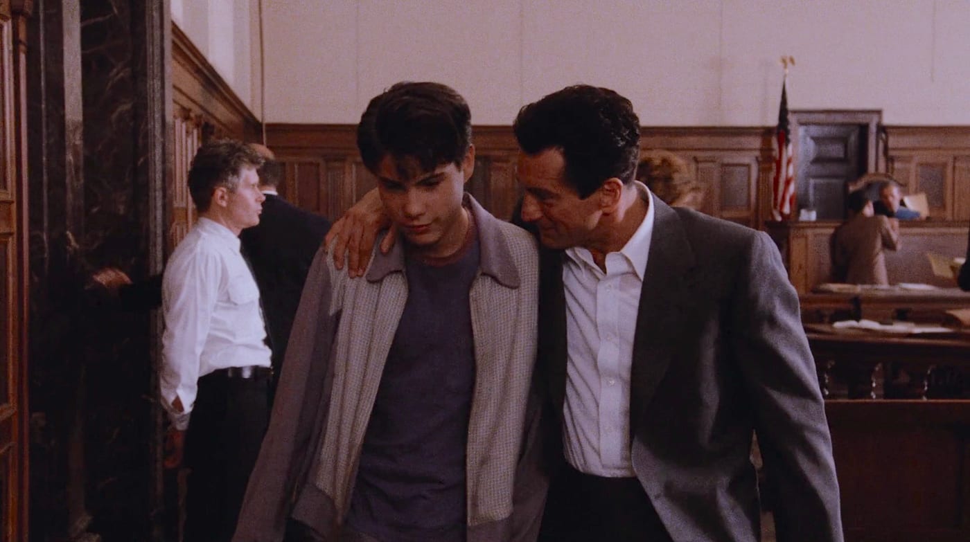 Robert De Niro as Jimmy Conway, his arm around a teenage Henry Hill in a courtroom in Goodfellas.