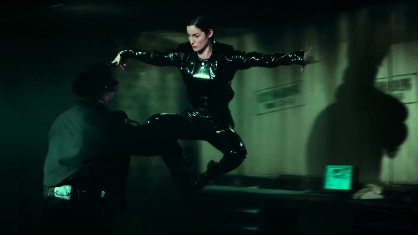 Trinity from The Matrix hangs frozen mid-air, knee raised, about to kick a police officer.