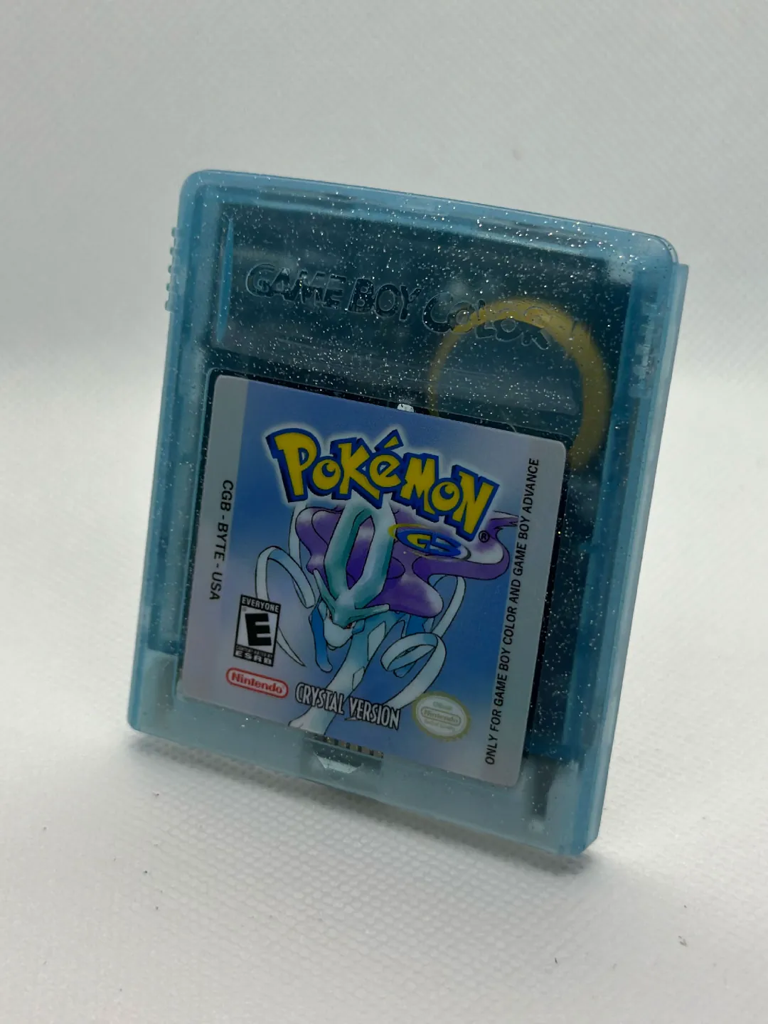 A translucent, glittery blue Pokémon Crystal cartridge standing on a white surface